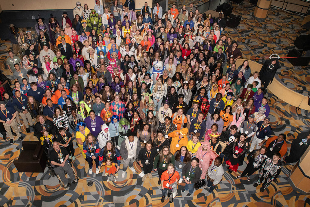 A large group of people dressed in various costumes, gathered together in a spacious indoor area.