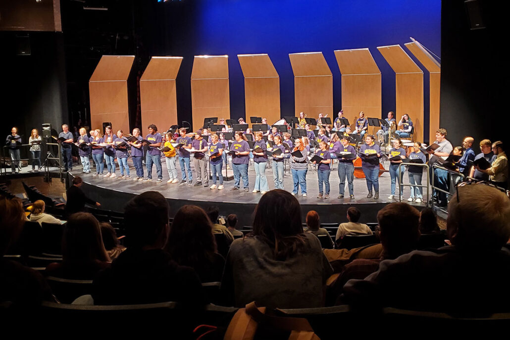 The UM-Flint Music University Chorale performs on stage for an audience