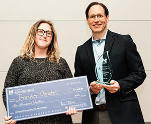 Two people holding a large check and a glass award, standing against a plain wall.
