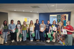 Group of people standing indoors holding papers and green gift bags, next to a "Life Skills" banner.
