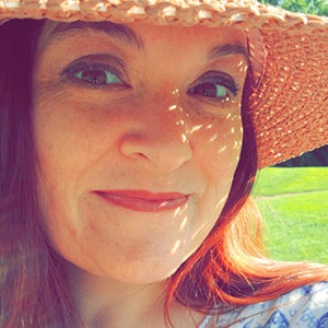 A person wearing a wide-brimmed straw hat outdoors with green grass in the background.