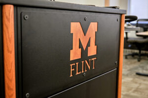 University of Michigan-Flint logo on a black and wood podium in an office setting.