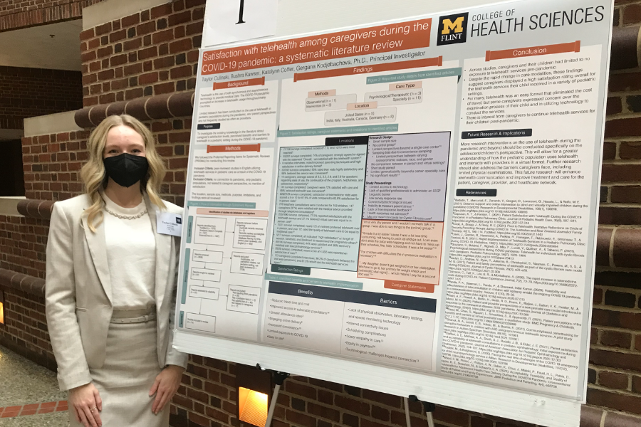Culinski poses in front of presentation board at the Undergraduate Research Symposium in Ann Arbor