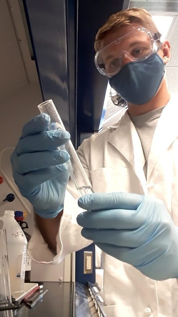 Thelen examines a sample in the laboratory. He is wearing a lab coat and full personal protective ewquipment.