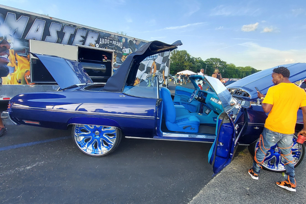 A few folks gather around a flashy blue Donk soft-top convertible next to the Donkmaster race trailer. It's one of Sage Thomas' Donks.