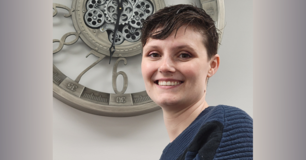 Picture of Angela standing in front of gray wall with a clock