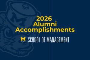 A navy-blue graphic with the phrase "2026 Alumni Accomplishments" in yellow font. Below this phrase is the University of Michigan-Flint School of Management logo. The background is a gruff wolverine watermark.
