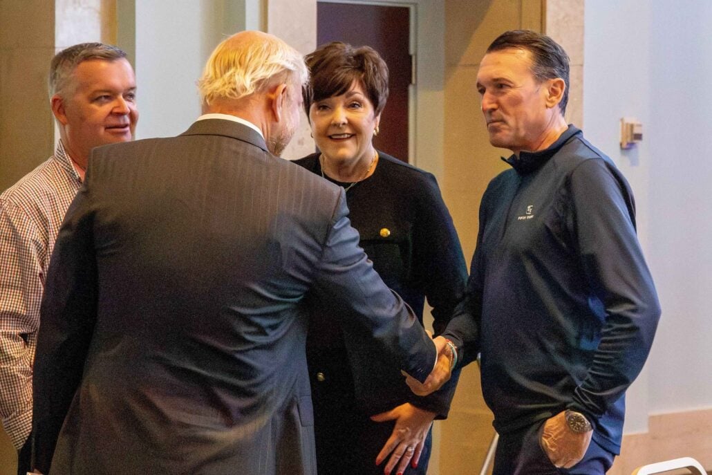 A group of four people are engaged in conversation. One man shakes hands with another man while others observe and smile.